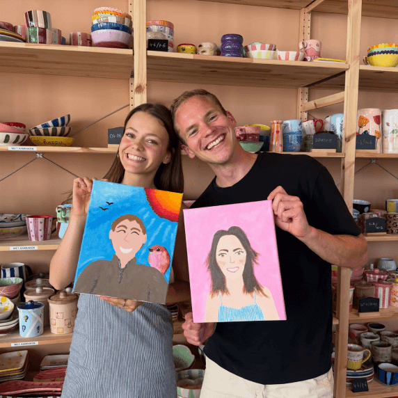 Two participants holding portrait paintings in an art studio